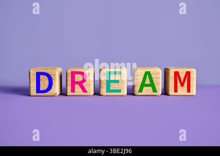 Das Wort TRAUM auf Holzblöcken auf leuchtendem lila Hintergrund mit bunten Buchstaben. Motivationskonzept Stockfoto