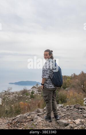 Wanderer steht auf einem felsigen Bergpfad mit Blick auf das Meer und die ferne Insel Stockfoto