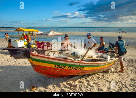 Brasilien, Nordeste, Ceara, Jericoacoara, Fischer vor ihrem farbenfrohen Boot am Strand bei Ebbe, in der Nähe eines fahrenden Caipirinha-Stands Stockfoto