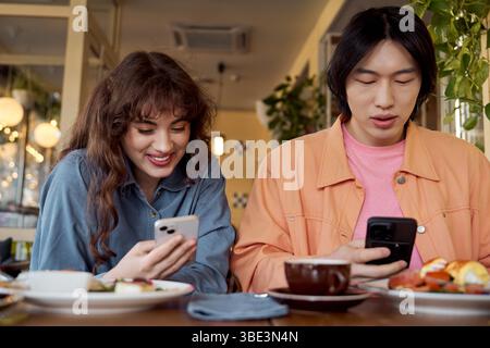 Zwei Freunde, ein asiatischer Mann und eine Kaukasierin, teilen einen freudigen Moment in einem Café. Stockfoto