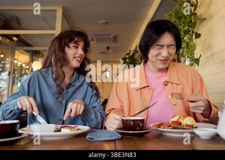 Zwei Freunde, ein junger Mann und eine junge Frau, genießen eine köstliche Mahlzeit mit einem Lächeln und einer Glückseligkeit. Stockfoto