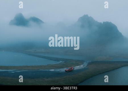 Nebel rollt über den Eystrahorn Berg, während ein roter SUV an der Küste in Ost-Island parkt. Stockfoto