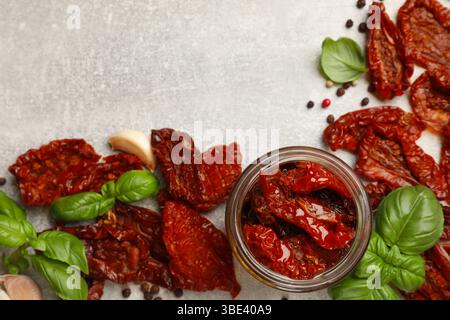 Köstliche sonnengetrocknete Tomaten im Glas und Gewürze auf grauem, strukturiertem Tisch, flach gelegen. Leerzeichen für Text Stockfoto