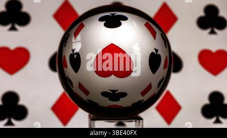 Gebrochenes oberes Herz durch eine Linsenkugel, umgeben von Spielkartensymbolen, Diamanten, Spaten und Schlägern. Stockfoto