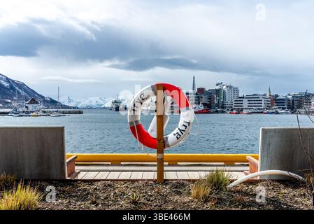 Tromsø, Norwegen. Ein Rettungsschirm mit der Stadtlandschaft von Tromso, schneebedeckten Bergen und Sportbooten, Yachten und Schiffen im Hintergrund Stockfoto