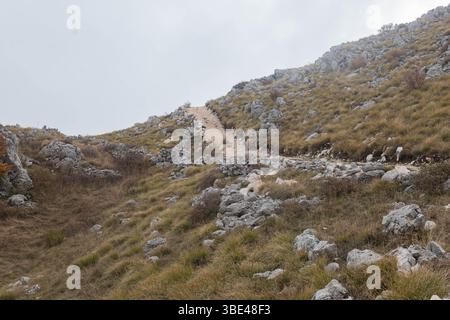 Felsiger Wanderweg schlängelt sich durch steile alpine Hügel mit karger Vegetation Stockfoto