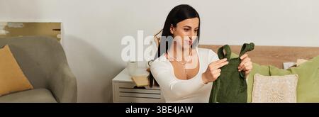 Schöne junge Frau bewundert ein grünes Baby-Outfit in ihrem warmen und einladenden Wohnzimmer. Stockfoto