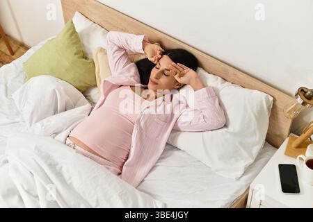 Die erwartende Mutter nimmt sich einen Moment, um sich an einem ruhigen Morgen in ihrem gemütlichen Schlafzimmer zu entspannen. Stockfoto