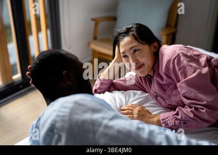 Glückliches und vielseitiges Paar, das einen fröhlichen Moment zu Hause teilt, zusammen umgeht und lächelt Stockfoto
