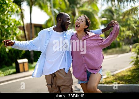 Glückliches, interrassisches Paar lacht zusammen draußen, genießt einen unbeschwerten Moment der Liebe, Freude Stockfoto