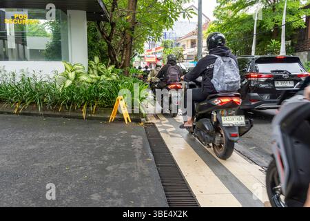 Bali, Indonesien - 23. Dezember 2024: Befahrene Straße mit vielen Motorrädern und Autos. Motorradfahrer fahren auf dem Fußgängerweg Stockfoto