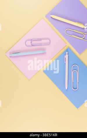 Draufsicht der rosafarbenen, lila und blauen Notizbücher auf gelbem Hintergrund. Pinkfarbene, gelbe und blaue Stifte, Büroklammern, Schule, Bürotapete. Stockfoto