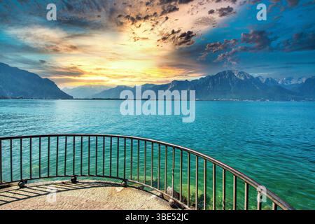 Goldenes Licht reflektiert das ruhige Wasser des Genfer Sees, während sich Wolken über den Bergen in Montreux, Schweiz, sammeln Stockfoto