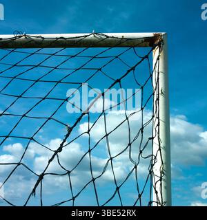 Ein Fußballtornetz befindet sich vor einem bewölkten Himmel und zeigt die komplizierten Details des Netzes. Das Sonnenlicht bricht durch Stockfoto