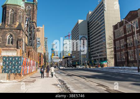 Urbane Straße in der Innenstadt von Toronto im Winter mit Fußgängern, historischen und modernen Gebäuden, Baukränen und klarem blauem Himmel. Stockfoto