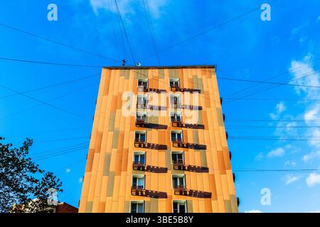 Orangefarbenes mehrstöckiges Wohngebäude und Stromkabel im blauen Himmel Stockfoto