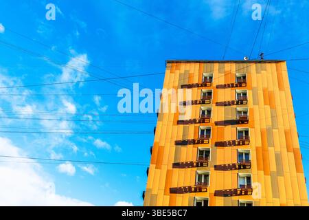 Orangefarbenes Apartmentgebäude und Stromkabel in blauem Himmel Stockfoto