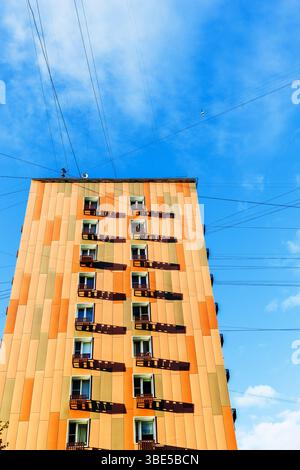 Orangefarbenes mehrstöckiges Stadthaus und elektrische Kabel und Kabel am blauen Himmel Stockfoto