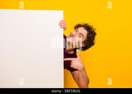 Junger, stilvoller Mann in burgunderrotem Polo, der kreativ vor hellgelbem Hintergrund zeigt und modernen Lebensstil zeigt Stockfoto