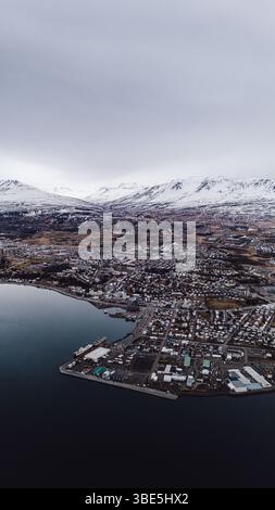 Drohnenblick auf Hofsos, ein kleines Küstendorf im Norden Islands, mit Hafen, Häusern und schneebedeckten Bergen im Hintergrund unter einem Ov Stockfoto