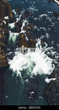 Drohnenaufnahme des Godafoss-Wasserfalls in Island, der die gekrümmte Formation von Gletscherwasser einfängt, das über dunkle Vulkangesteine in eine lebendige, Stockfoto