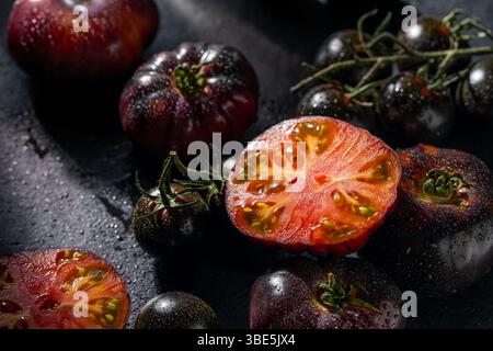 Eine Sammlung reifer, erblicher Tomaten mit satten Farben, glitzernd mit Wassertropfen auf dunklem Hintergrund. Die lebendigen Texturen und Erdtöne cr Stockfoto