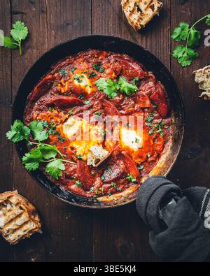 Ein köstliches Shakshuka-Gericht mit reichhaltiger Tomatensauce und perfekt gekochten Eiern, garniert mit frischen Kräutern, präsentiert in einer rustikalen Pfanne, ideal für Stockfoto