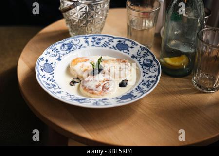 Hüttenkäsepfannkuchen mit cremiger Sauce, Heidelbeeren und Minze auf einer dekorativen Porzellanplatte. Stockfoto