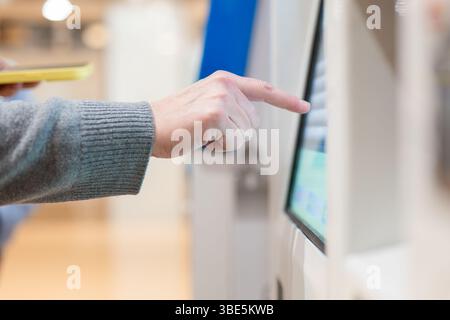 Nahaufnahme der Hand einer Person, die mit einem Touchscreen-Kiosk an einem Flughafen interagiert. Das Bild betont moderne Technologie und Komfort für Trav Stockfoto