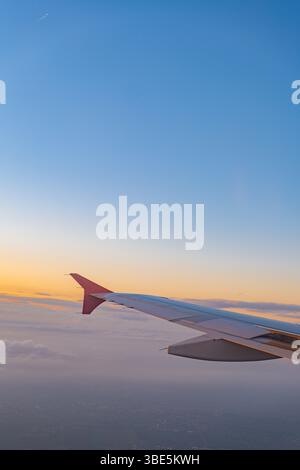 Eine malerische Aussicht aus einem Flugzeugfenster, die den Flügel des Flugzeugs vor einem atemberaubenden Sonnenunterganghimmel hervorhebt. Dieses Bild zeigt das Wesen von Air trave Stockfoto