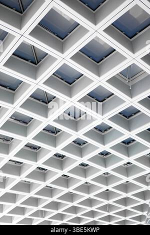 Die moderne Flughafendecke verfügt über ein geometrisches Gitter aus Oberlichtern, das ein Muster aus Licht und Schatten erzeugt. Dieses architektonische Design verbessert die Reise Stockfoto