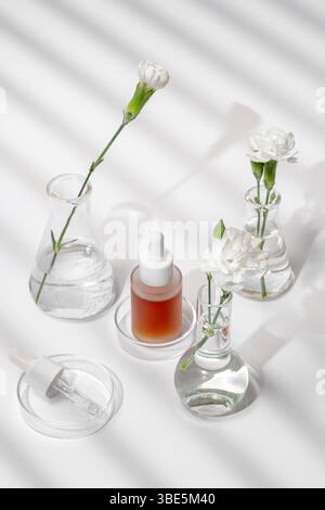 Von oben eine ruhige Einrichtung aus Hautpflegeprodukten und frischen Blumen in Laborgläsern, die unter sanften Lichtverhältnissen und Schatten erfasst werden. Ideal für Hochglanz Stockfoto
