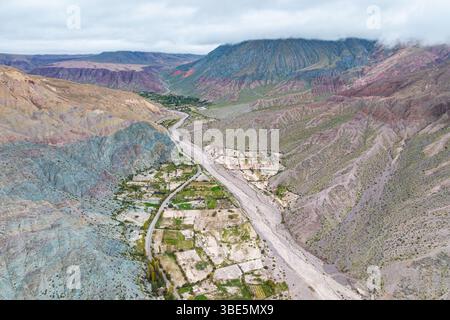 Aus der Vogelperspektive auf Purmamarca, Jujuy, Argentinien, mit lebendigen, bunten Bergen, die ein malerisches Tal umgeben. Wolken schweben über dem lebendigen Stockfoto