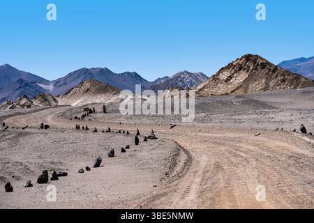 Eine einsame Straße schlängelt sich durch das felsige, trockenes Gelände von La Puna, Argentinien, umgeben von zerklüfteten Bergen unter einem klaren blauen Himmel. Stockfoto