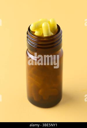 Eine braune Flasche gefüllt mit gelben Kapseln auf einem durchgehend gelben Hintergrund. Der Farbkontrast betont den Inhalt, hebt Gesundheit und hervor Stockfoto