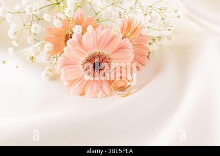 Elegante Nahaufnahme goldener Eheringe auf sanften rosafarbenen Gänseblümchen, umgeben von Babyblüten, die Liebe und Engagement in einer romantischen Atmosphäre symbolisieren Stockfoto