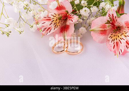 Nahaufnahme zweier eleganter Eheringe neben leuchtenden Lilien und zarten Babyblüten, die Liebe und Feier auf einem besonderen d symbolisieren Stockfoto