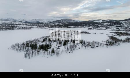 Atemberaubende Aussicht aus der Luft, die eine schneebedeckte nordische Landschaft mit dichten Wäldern und fernen Bergen einfängt. Die ruhige Winterszene zeigt unberührte Schönheit A Stockfoto