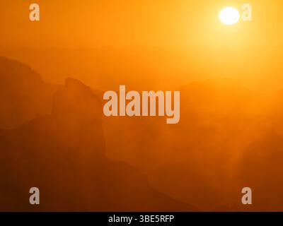Ein faszinierender Blick auf den Roque Nublo unter einem goldenen Sonnenaufgang, mit Silhouetten von Bergen, die von einem nebeligen, ätherischen Leuchten auf Gran Canaria umgeben sind. Stockfoto