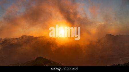 Majestätischer Blick auf den Sonnenuntergang hinter einem Wolkenschleier über den bergigen Landschaften des Dorfes Cruz de Tejeda auf Gran Canaria, der ein warmes „Go“-Erlebnis erzeugt Stockfoto