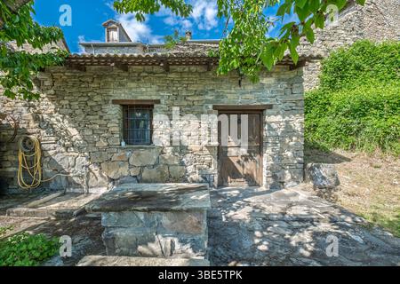 Rustikale Steinfassade mit Holztür und Fenster in ländlicher Umgebung. Traditionelle Architektur, Landschaftsszene, Grün, ländliches Leben Stockfoto