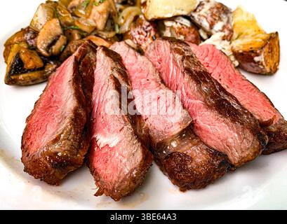 In Scheiben geschnittenes mittelseltenes Steak mit Pilzen und gerösteten Kartoffeln. Stockfoto