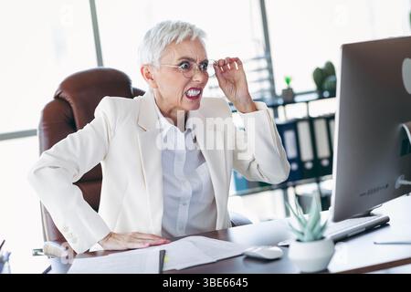 Frustrierte Geschäftsfrau, die im Büro arbeitet und gleichzeitig die Herausforderungen am Arbeitsplatz bewältigt, indem sie formelle Kleidung und Brille trägt Stockfoto