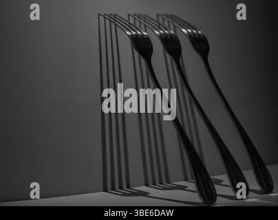 Drei Metallgabeln werfen scharfe, rhythmische Schatten gegen eine Wand in einer minimalistischen Stillleben-Komposition, die Symmetrie, Wiederholung und Licht betont. Stockfoto