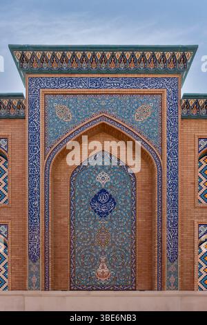 Traditionelle islamische Architektur mit spitzem Bogeneingang mit dekorativen blauen Fliesen, die eine elegante Fassade in A'ali schaffen. Stockfoto