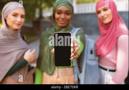 Drei Muslimische Frauen Zeigen Smartphone-Bildschirm Im Freien, Fokus Auf Telefon Stockfoto