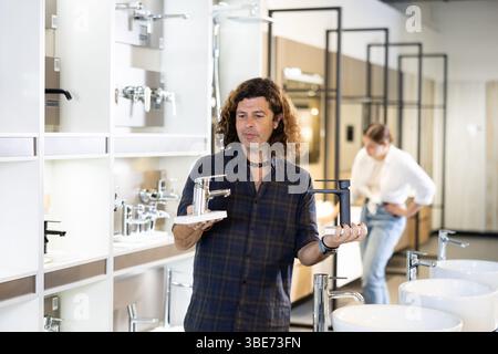 Ein Mann inspiziert und wählt einen neuen Küchen- oder Badezapfhahn im Baumarkt aus Stockfoto