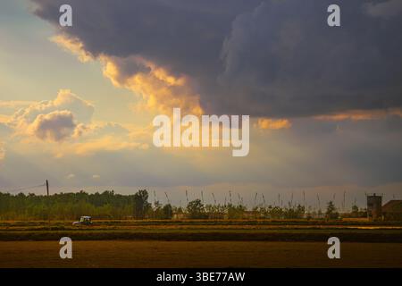 Sonnenuntergangsszene über Ackerland mit Traktor unter dramatischem Himmel Stockfoto