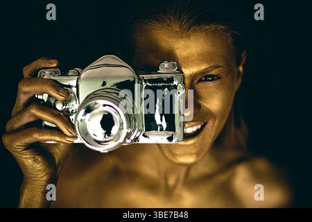 Porträt einer schönen jungen Frau, gemalt Gesicht und Haut Gold und hält Keramik Silber Kamera Statue zur Dekoration, während Sie schauen und glücklich lächeln Stockfoto