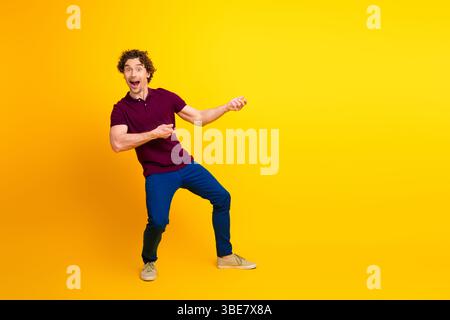 Energiegeladener junger Mann, der dynamisch vor einem hellgelben Hintergrund Gesten gibt und Stil und lässigen Charme zeigt Stockfoto